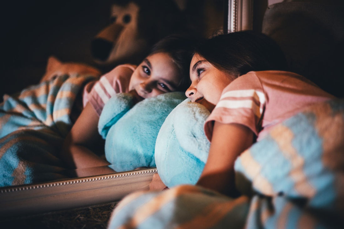 A child sitting in a cozy, warmly lit bedroom holding a stuffed animal, surrounded by calming bedtime items