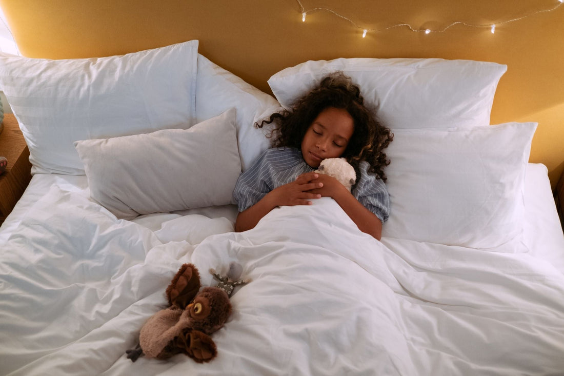 A young girl sleeping peacefully in a cozy bed, hugging a small plush toy, with warm string lights glowing softly above her headboard
