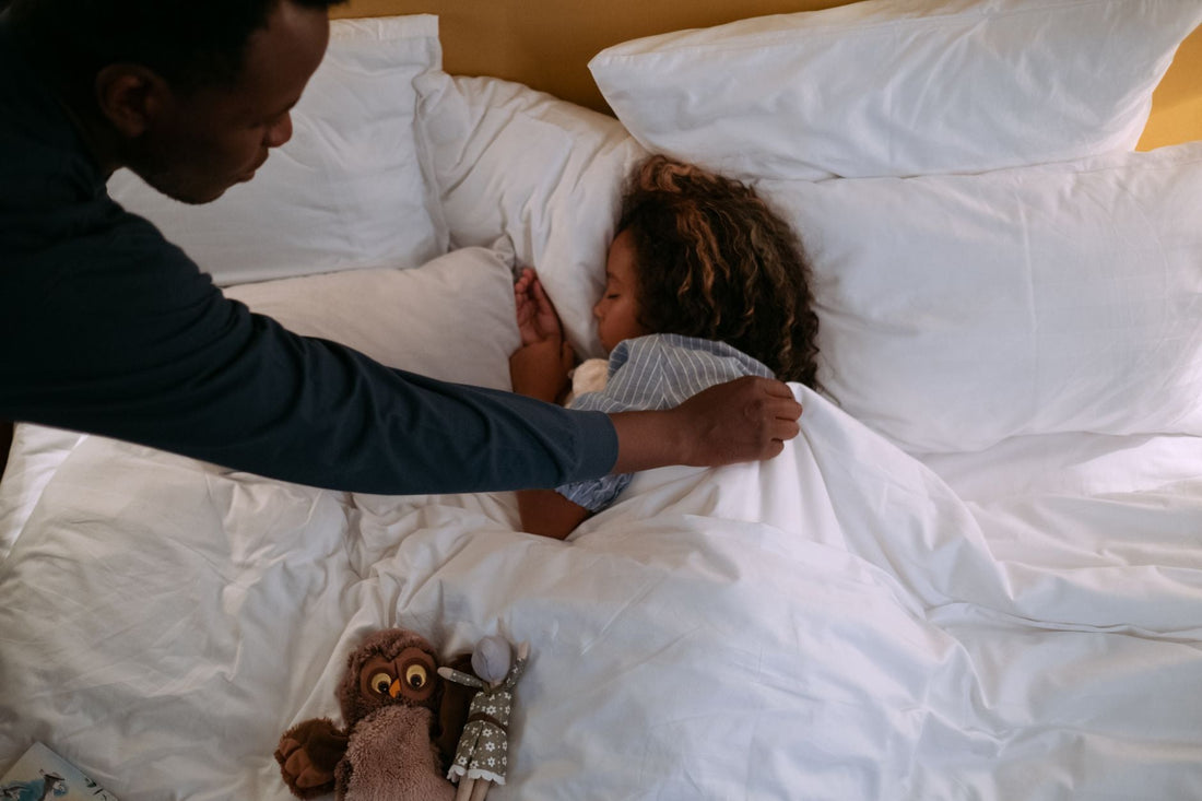 A parent sitting beside a child in bed at night, offering comfort after a nightmare